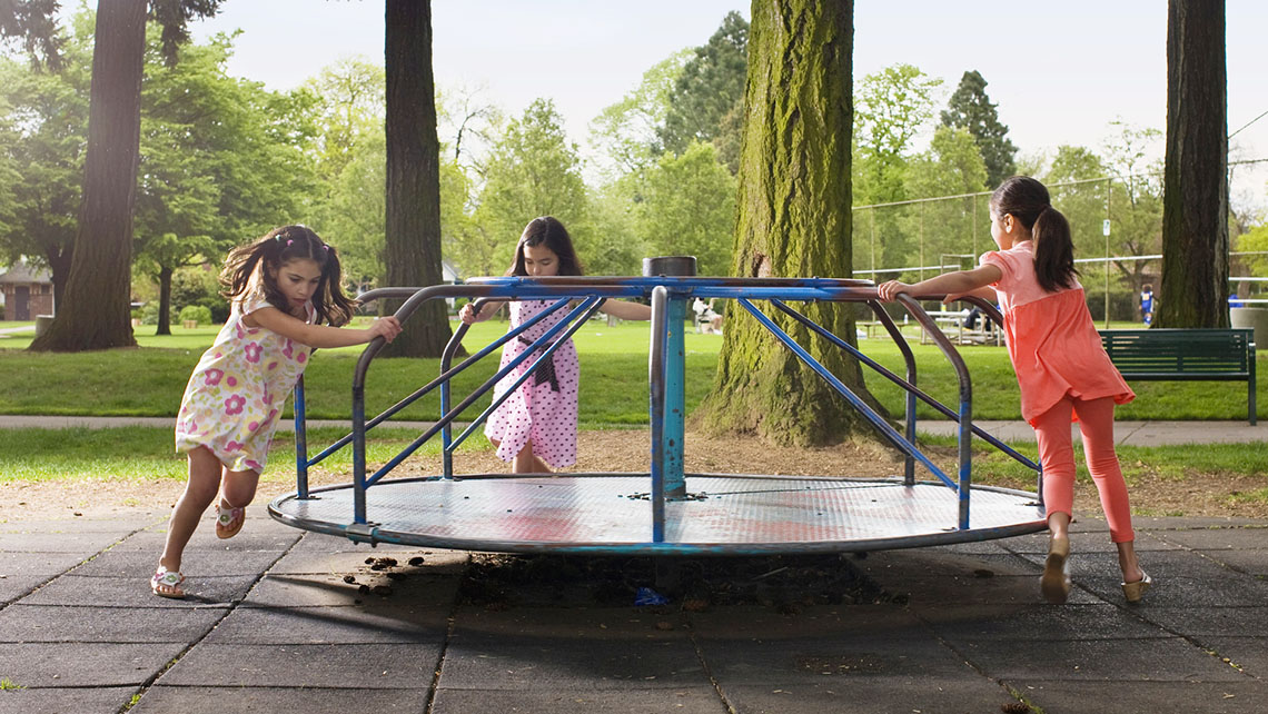 Playground forces 3 girls pushing a spinner at the playground outside
