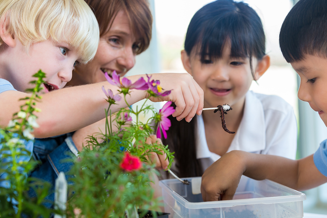 Three children and an adult examining a worm.
