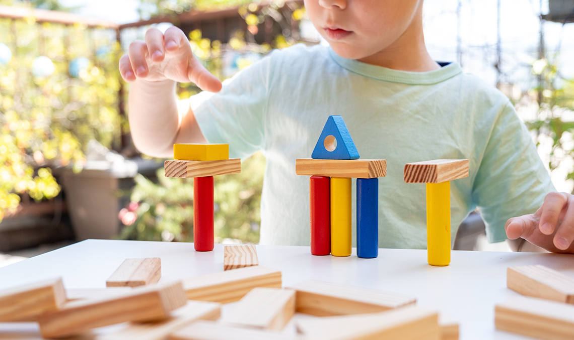 A child building a colourful structure using various 3 D blocks such as a cylinder, triangular prism