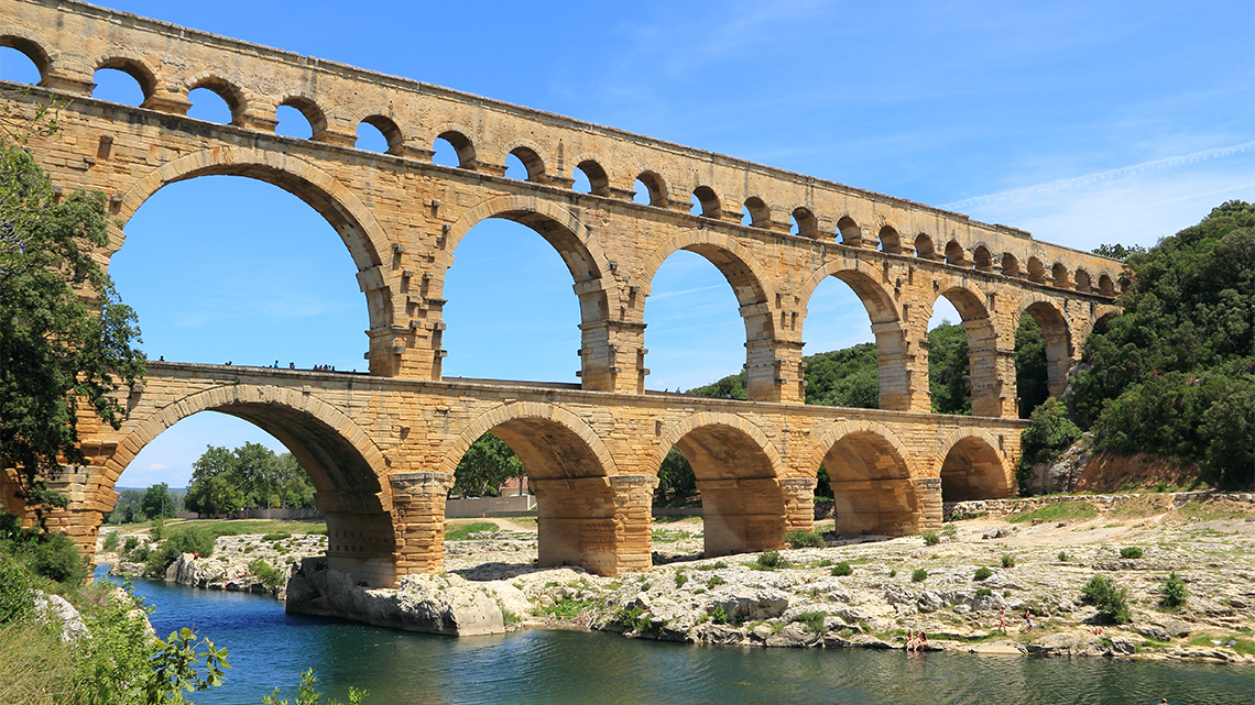 A three-tiered stone bridge crossing a river. The two lower tiers are made of large arches and the highest tier is made of small arches.