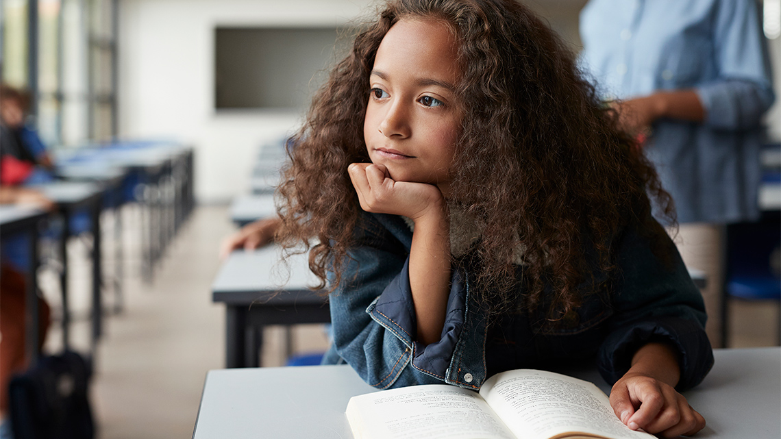 A student in class with a book open and her hand on her chin , thinking