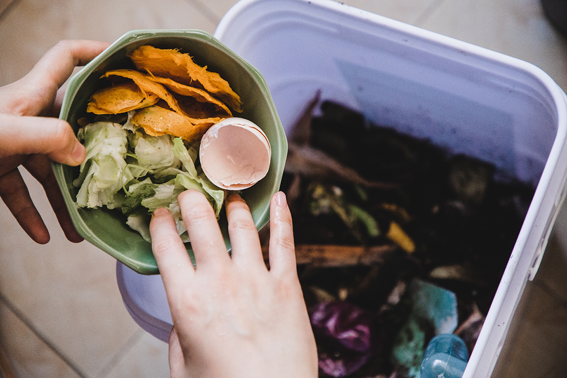 A person dumping organic food scraps into the compost bin.
