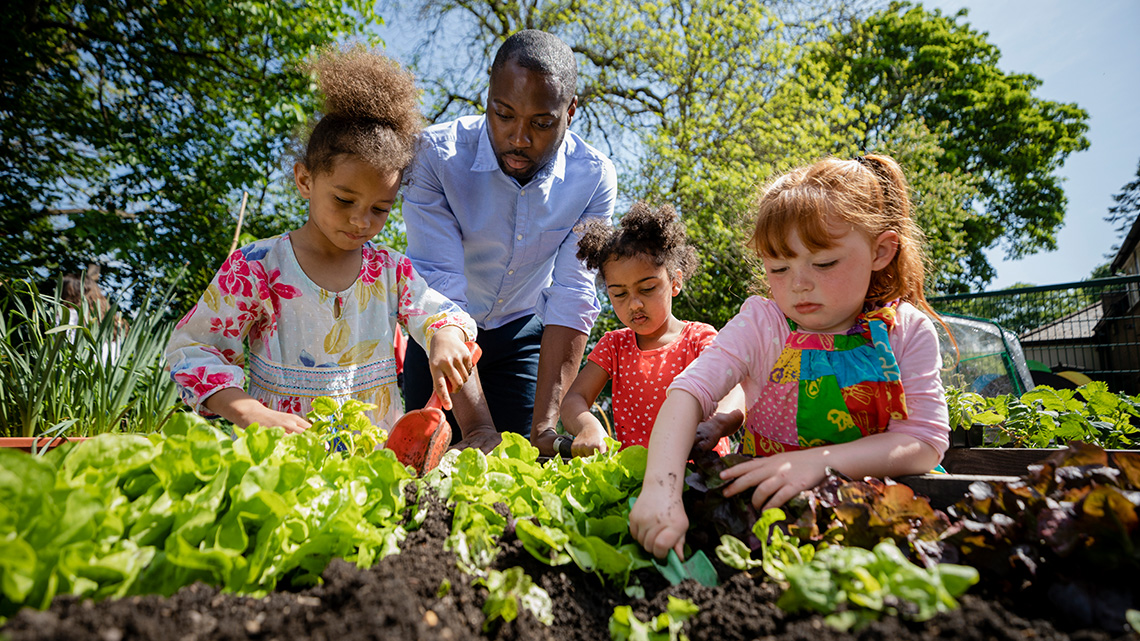 Three children and an adult planting a garden.