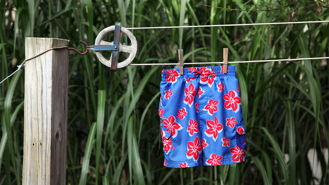 A clothesline made of a loop of cable and a small wheel hung on to a squared wood pole with a hanging swim short.
