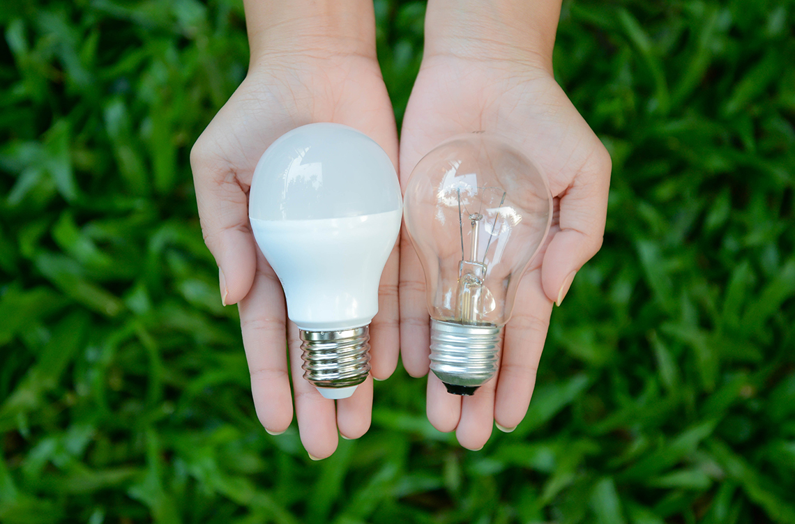 A person holding an incandescent light bulb on the left and an LED light on the right.
