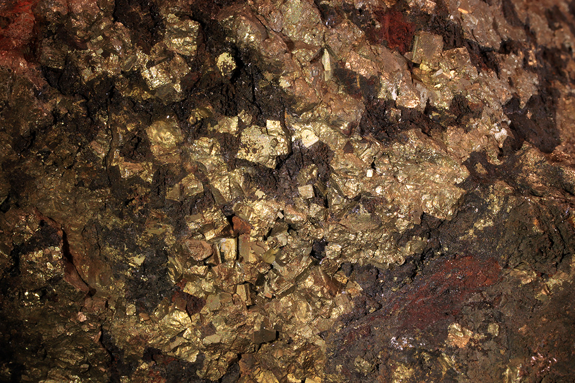 Shiny deposits of either gold, nickel, or silver cuts through the side view of an exposed chunk of bedrock.