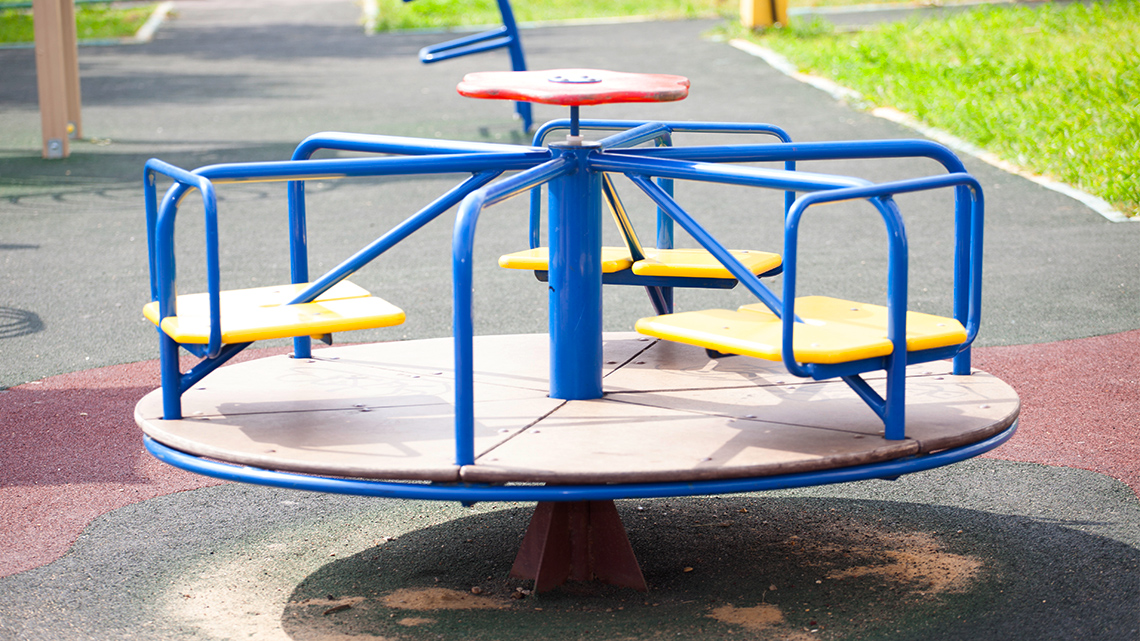 A metal merry-go-round is covered in rain in a park.