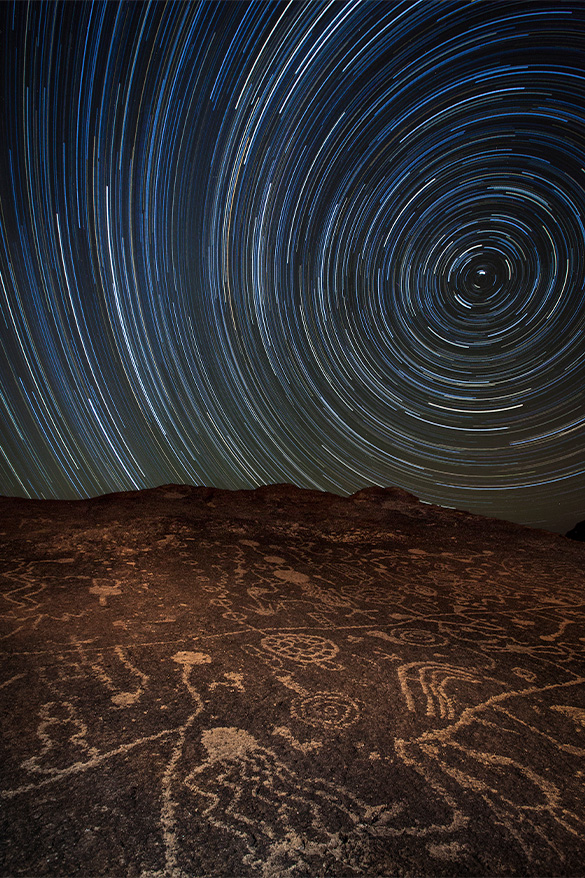 A large rockface covered in ancient stone carvings known as petroglyphs beneath the night sky.