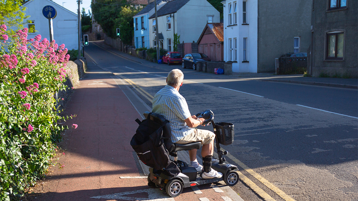 A person on a disability scooter stops at the edge of the pavement checking for safety before he drives his scooter across a road.