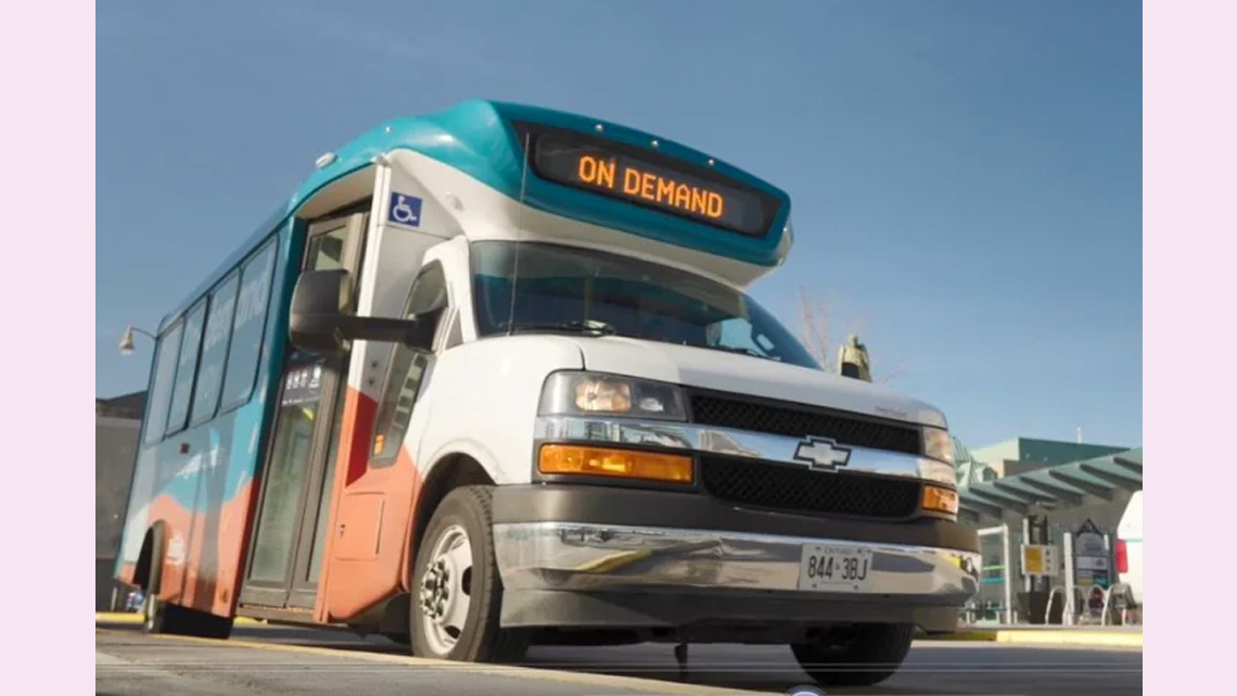 A bus is parked next to a gas station. The screen at the top of the bus reads “on demand”.