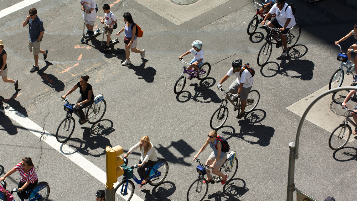 People walk and bicycle across a street during the daytime.