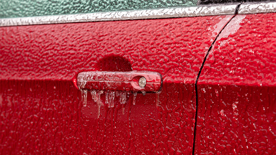 Frozen car There is a car door that is covered in ice. There are small articles hanging from the handle that opens the door and the car window.