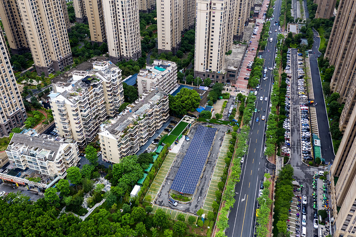 Aerial view of a city block. There are buildings, cars along the street and a public parking garage covered with solar panels.