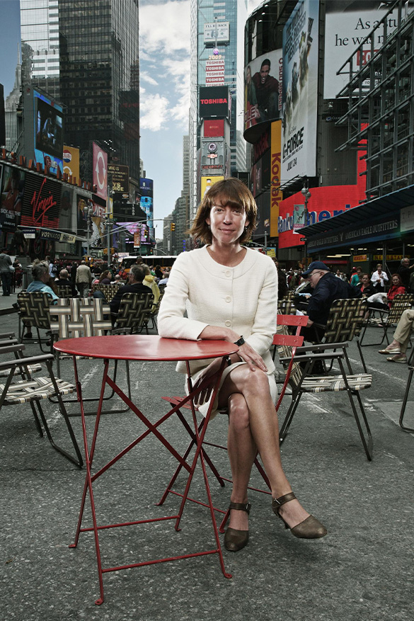 A portrait of Janette Sadik-Khan sitting at a table in the middle of Times Square.