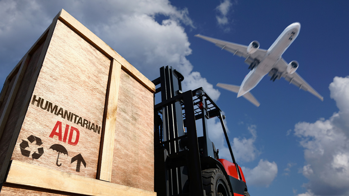 A forklift carrying a wooden box that has Humanitarian Aid stamped on it. A plane flies overhead.