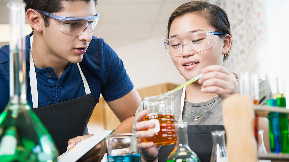 Two students mixing liquids in a beaker.