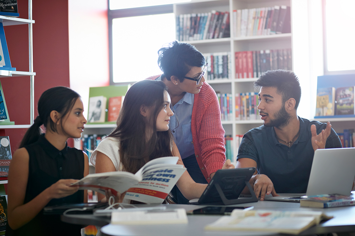 Three students talking with their teacher in the library.