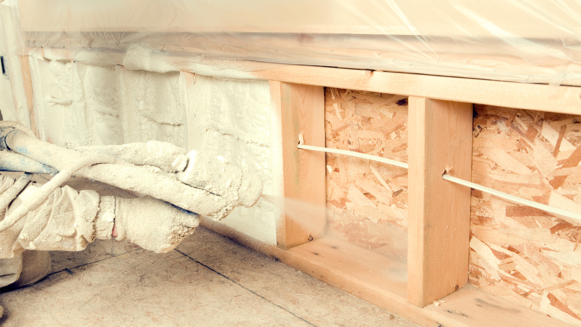 Insulation sprayed into a space between wooden joists in a wall.