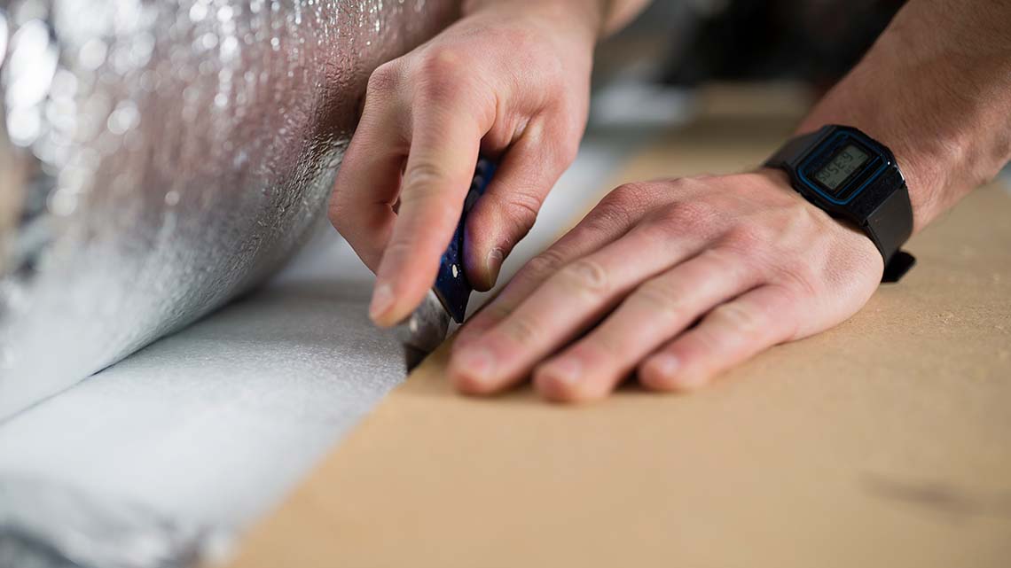 A person using a box cutter to cut through insulation.