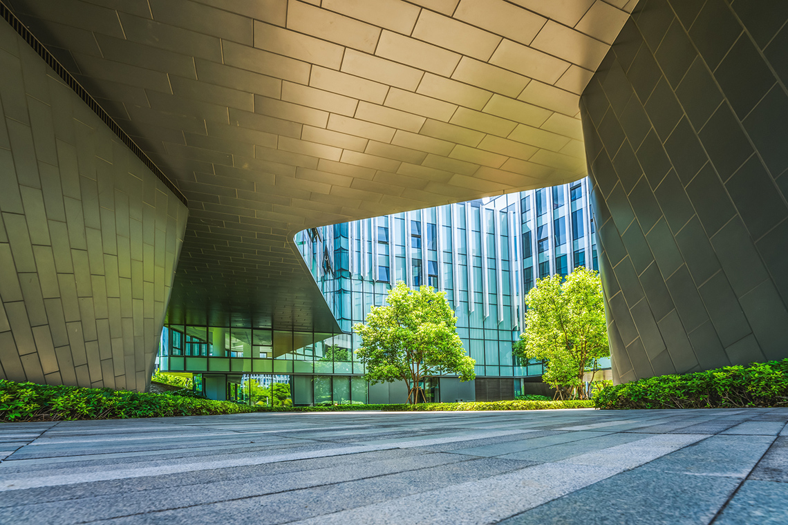 A building with a tunnel providing shade. There are trees and bushes lining the tunnel and building.