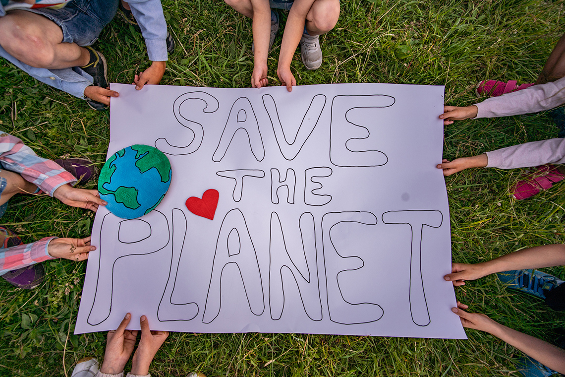 People holding a poster above the grass. The poster is titled Save the Planet.
