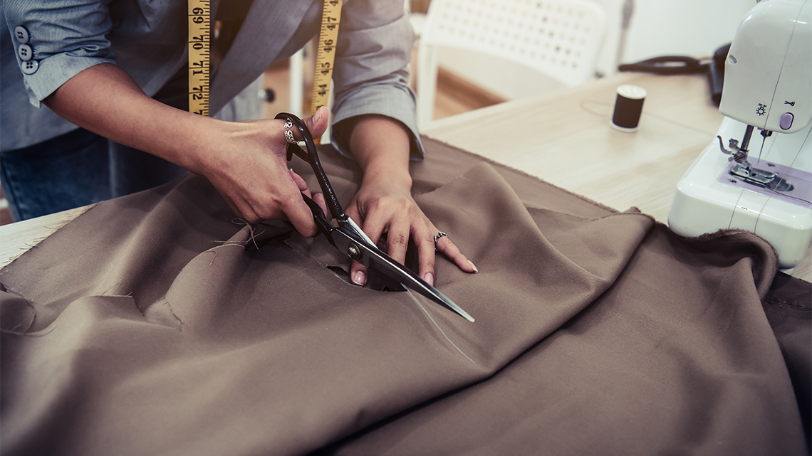 Dressmaker cutting, sewing, and measuring garment.