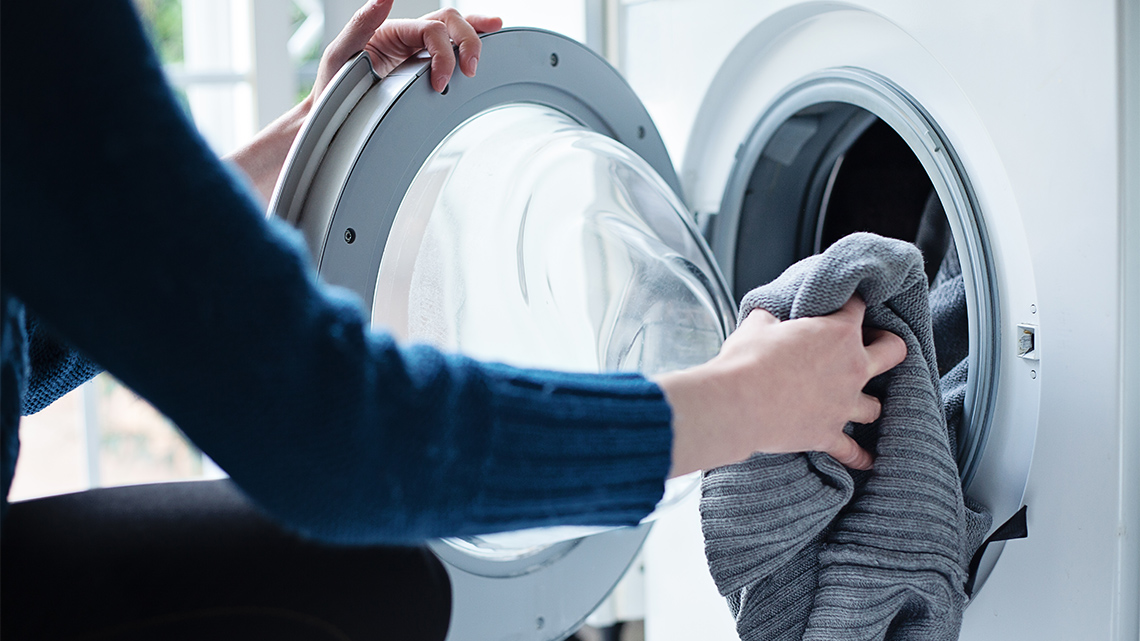 Person adding their clothes to the washing machine.