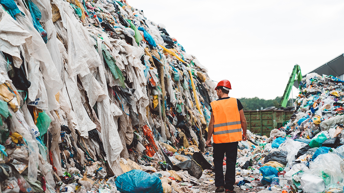 Person walking in between piles of garbage to be in the landfill.