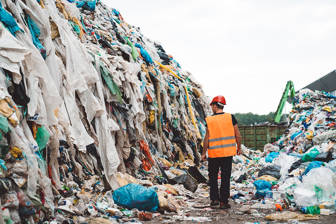 A person walking between piles of clothing waste and garbage.
