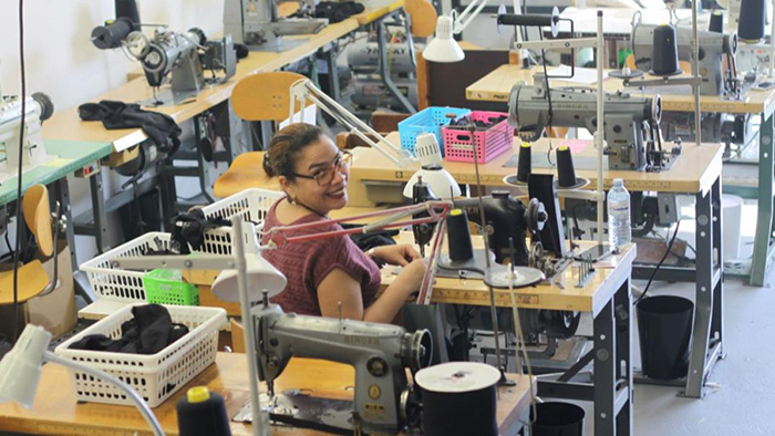 A person sitting behind a table using a sowing machine