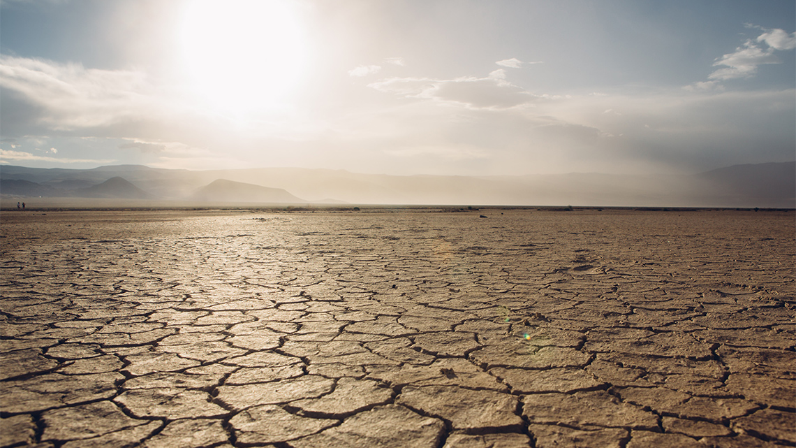 Barren desert with brown cracked clay in the foreground and mountains in the background.
