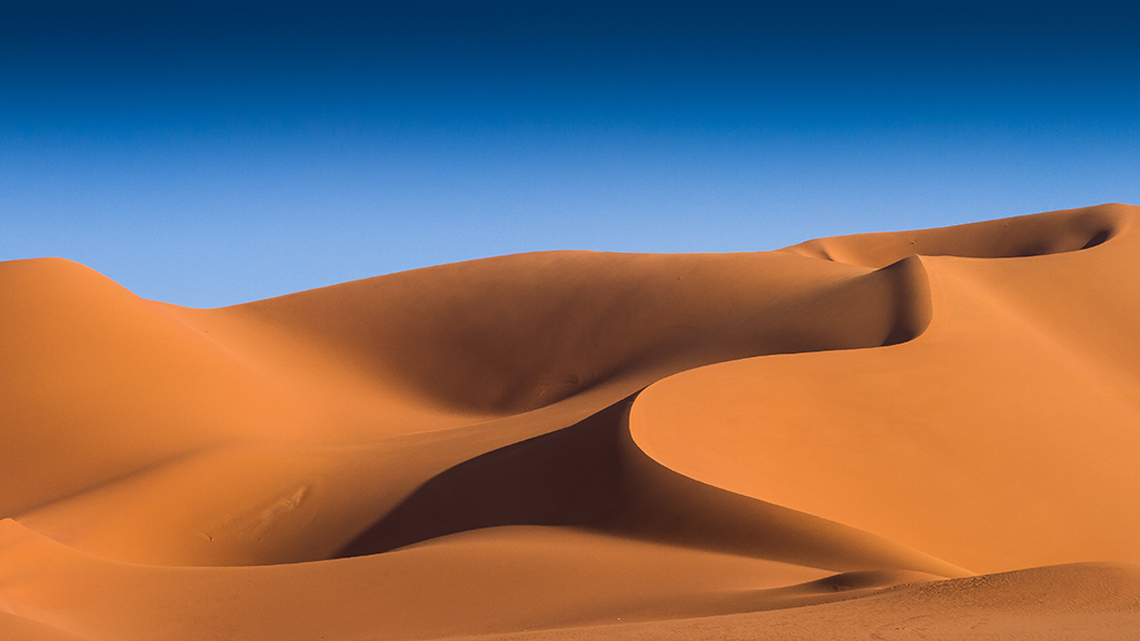 Many levels of sand dunes in the desert with a clear sky in the background.