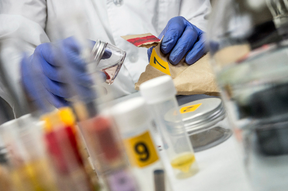 A forensic analyst’s gloved hands are pictured examining a blood sample from a paper bag with a yellow numbered label.