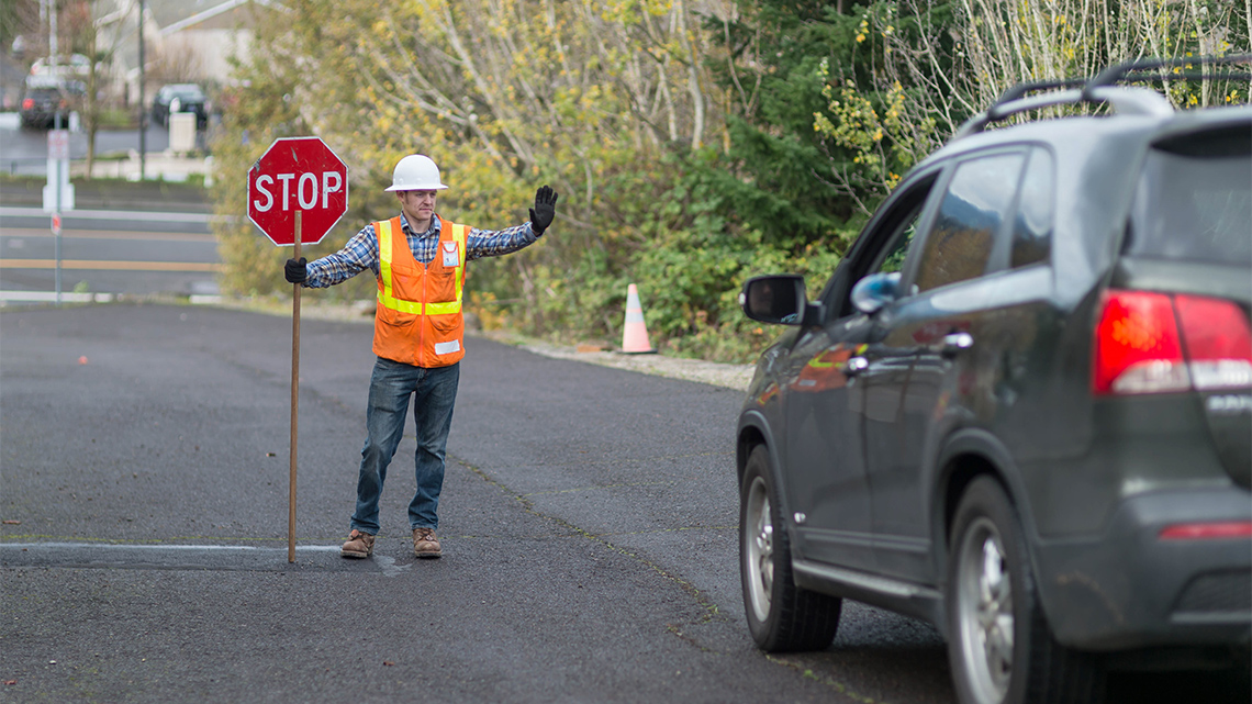 A construction worker holds up a stop sign and a car brakes to a stop in front of it.