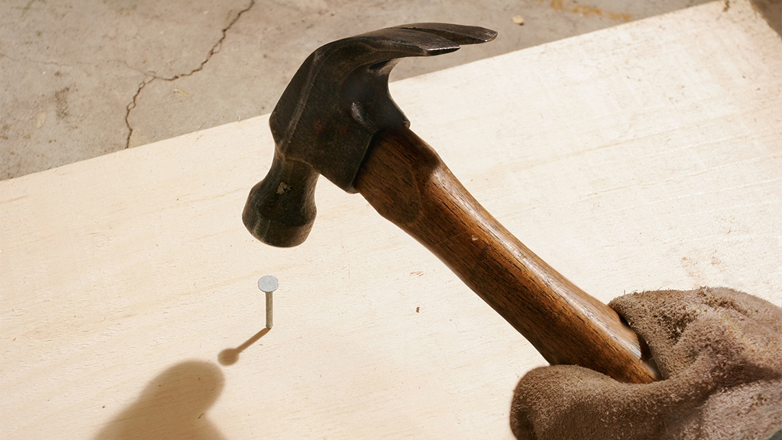 A hammer hitting a nail into a piece of wood.