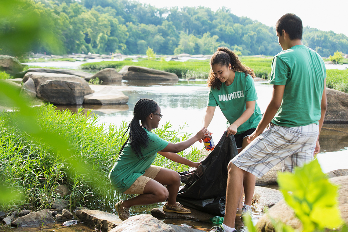 Three volunteers picking up garbage around a river.