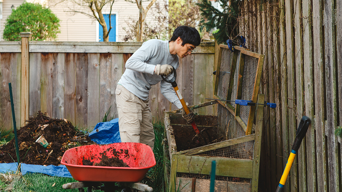 A person mixing the contents of a backyard composter.