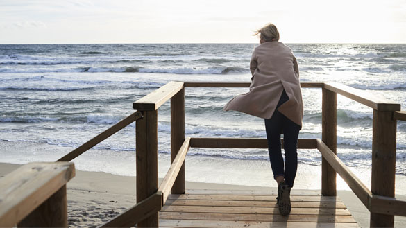 A person wearing a sweater as they lean against a railing and look out at the ocean.