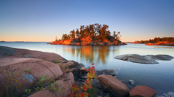 A body of water, with small rocky landforms coming up from the water, and an small island in the distance.
