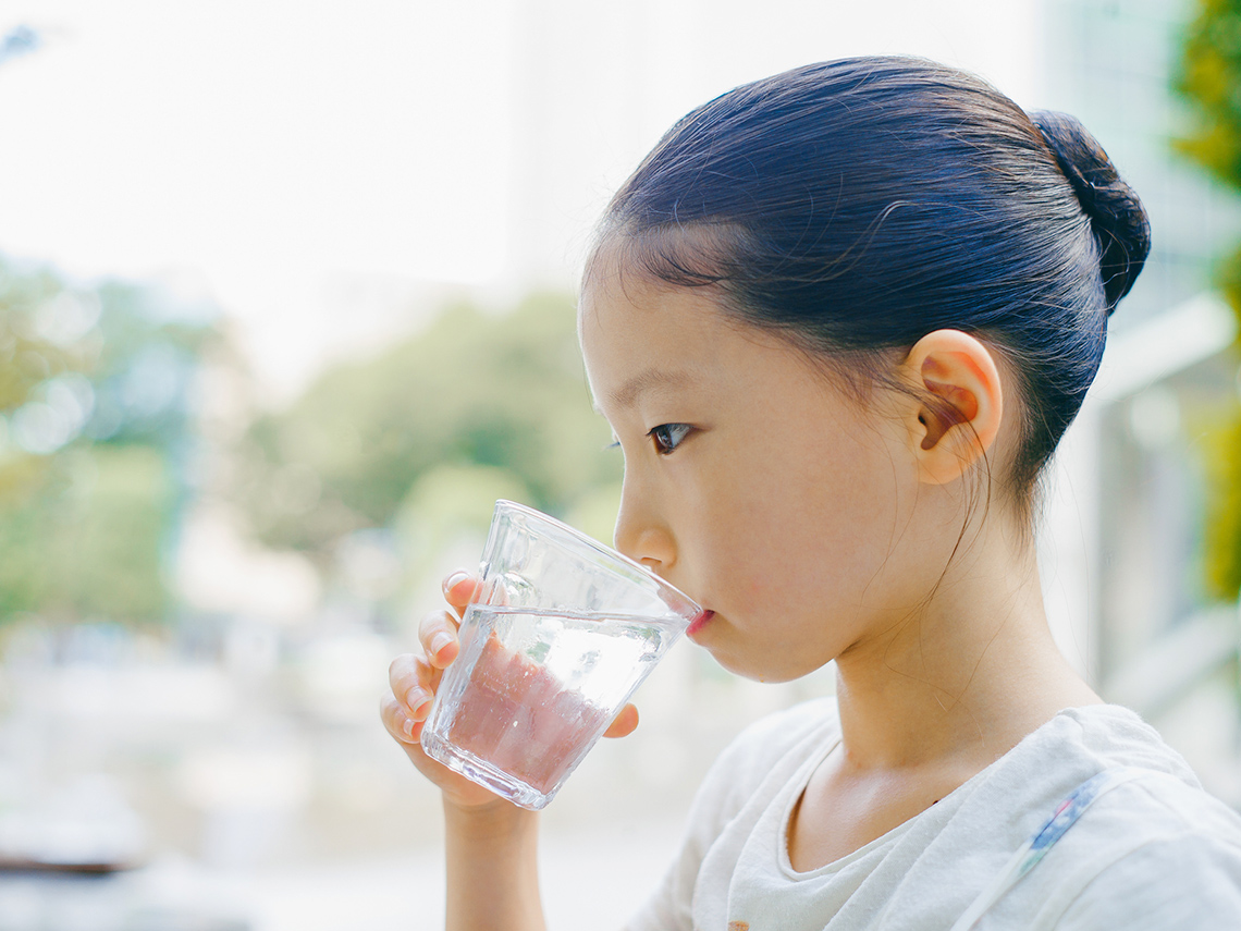 A child is drinking from a glass of water.