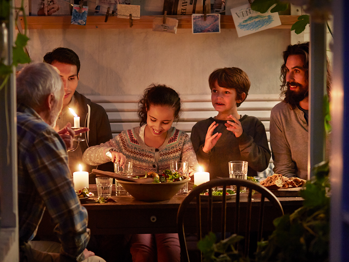 Children and adults sitting at a table that has food and water. They are eating.