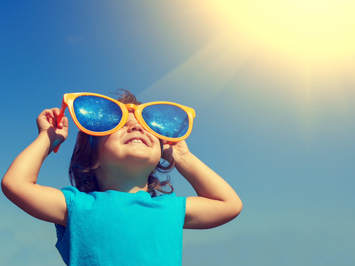 A child wearing very large sunglasses with the sun shining behind them.