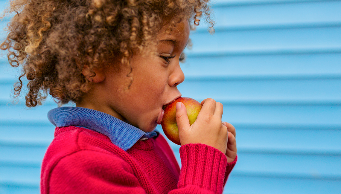 A child is holding an apple to their mouth and their lips are open.