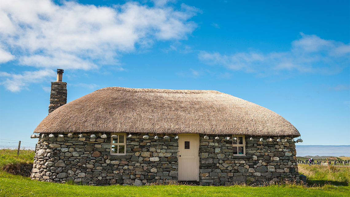 An old home built from stone that uses straw for its roof.