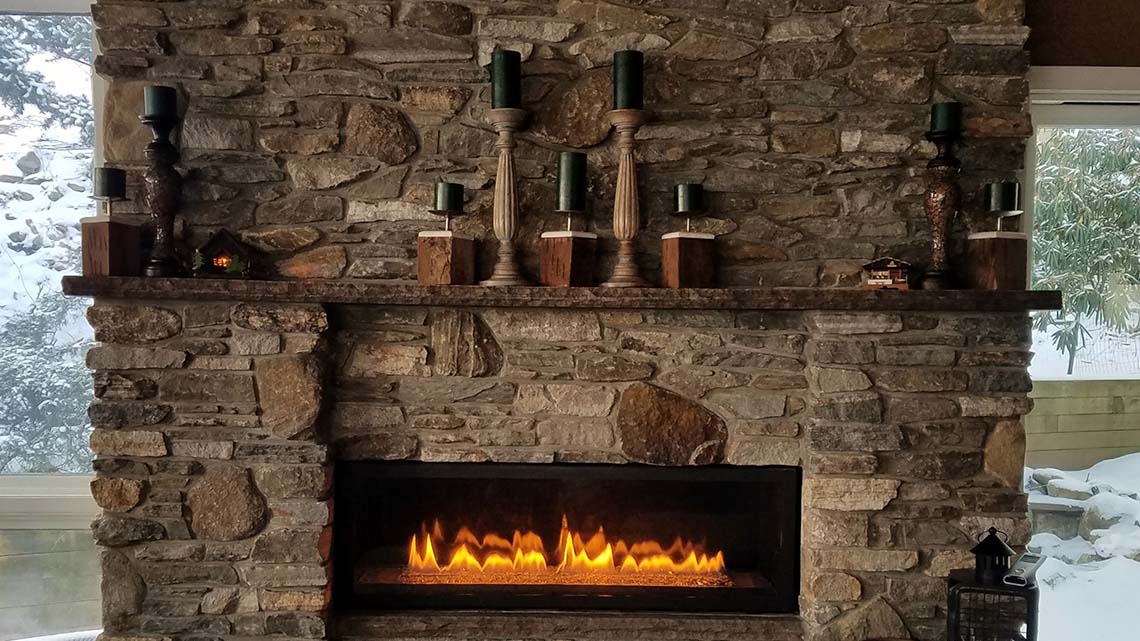 A fireplace inside a home that is made of rocks and stones. It has a wooden mantle with wooden candlesticks and candles.