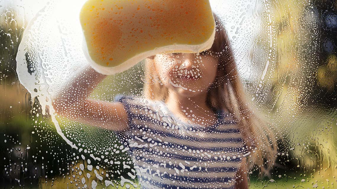A learner using soapy water and a sponge to clean a window.