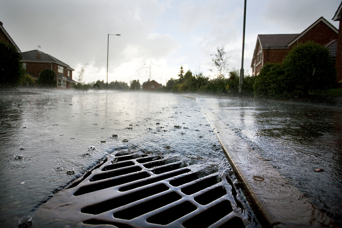 Rainwater running into a storm drain on the side of a road in a neighbourhood.