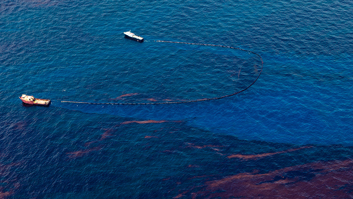 Two boats are skimming oil from the surface of the water.