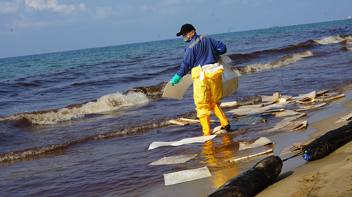 A person uses pads to soak up oil on a beach.