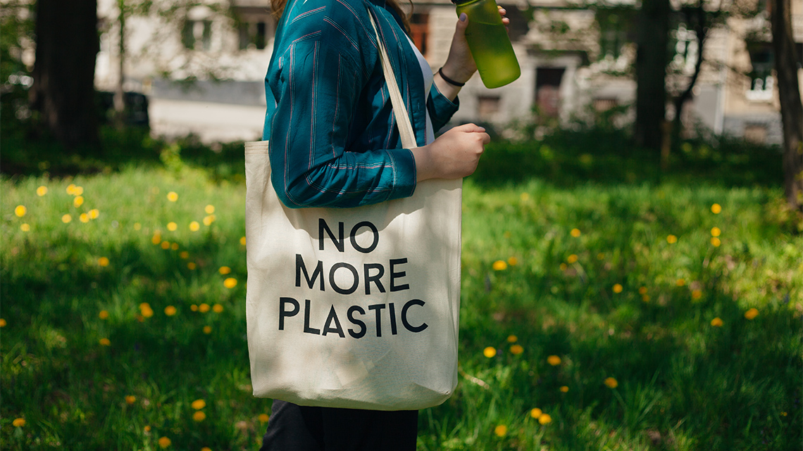 Person using a reusable canvas bag. The text design on the bag reads ‘No more plastic.’